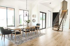 a dining room table with chairs and a stair case in front of glass doors that lead up to the second floor