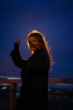 a woman standing on top of a balcony next to a sky filled with clouds at night