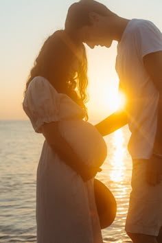 a man and woman standing next to each other in front of the ocean at sunset