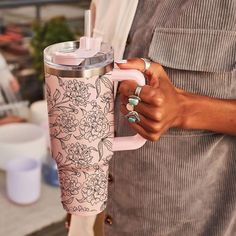 a woman holding a pink coffee cup in her right hand and thermos on her left