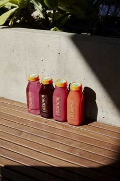 four juice bottles sitting on top of a wooden bench