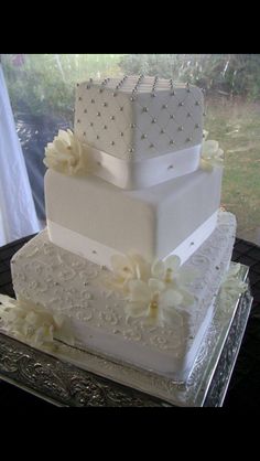 a three tiered wedding cake with white flowers on the side and pearls at the top