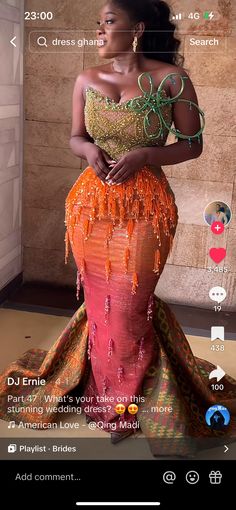 a woman in an orange and green dress with beads on her head, standing next to a wall