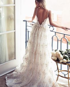 a woman in a wedding dress standing on a balcony looking out the window at flowers