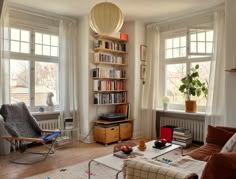 a living room filled with furniture and bookshelves next to two large open windows