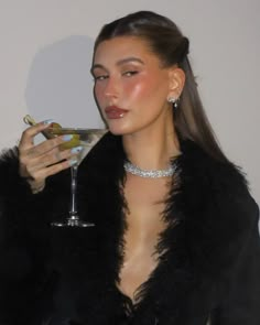 a woman holding a martini glass in her right hand and wearing a black fur coat