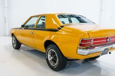 an old yellow car is parked in a white room with black rims and chrome wheels