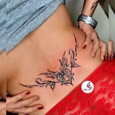 a woman's lower back tattoo with flowers and vines on the side, behind her belly