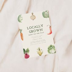 a baby on the way book sitting on top of a white bed sheet with vegetables printed on it