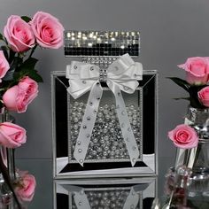 pink roses are in vases next to a silver box with pearls and bows on it