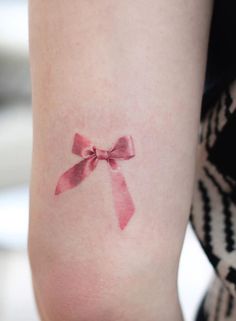 a woman's arm with a pink bow tattoo on the left side of her arm