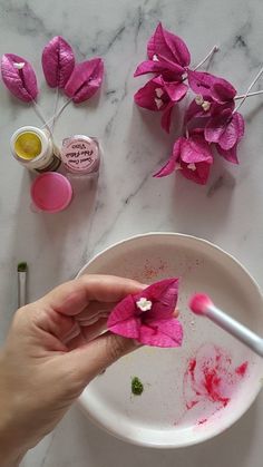 a person is painting flowers on a white plate with pink and green paint in front of them