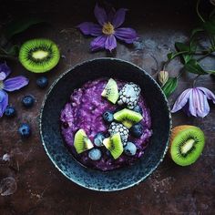 a bowl filled with blueberries and kiwi slices on top of a table next to flowers