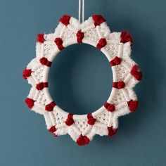 a red and white crochet wreath hanging on a blue wall