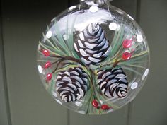 a glass ornament with pine cones and berries hanging from it's side