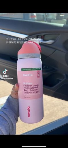 a person holding up a pink bottle in front of a car door with the words owala on it