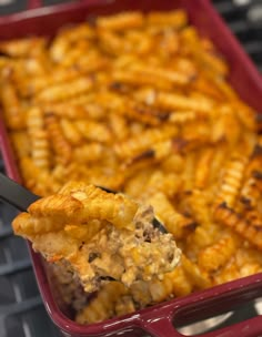 a spoon full of food sitting on top of a red container filled with macaroni and cheese