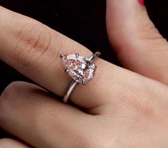 a woman's hand with a ring on it that has a pink diamond in the middle