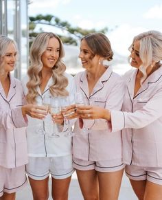 four beautiful women in pink pajamas holding wine glasses and smiling at each other while standing next to each other