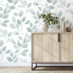 a wooden cabinet sitting in front of a wall with leaves painted on the wall behind it