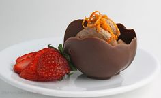 a chocolate egg shell with strawberries on the side and an orange garnish