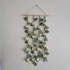 a crocheted wall hanging with white flowers and green leaves on a wooden stick