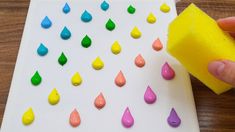 a person is using a sponge to paint drops on a paper board with yellow and pink colors