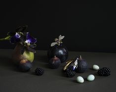 two vases with flowers and some fruit on the ground next to eggs in front of them