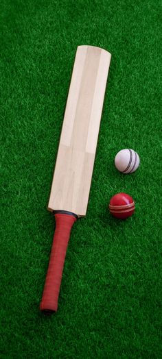 a wooden cricket bat and ball laying on the ground