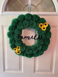 a green wreath with yellow daisies and the word family hanging on it's front door