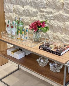 a glass table with bottles and flowers on it in front of a stone brick wall