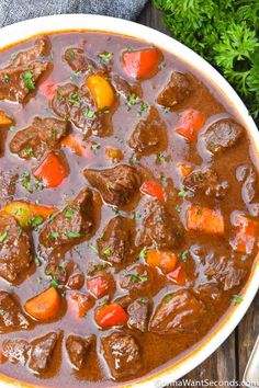 a bowl of beef stew with carrots and parsley