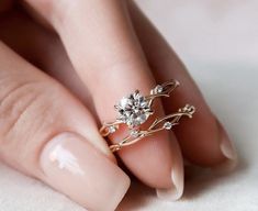 a woman's hand holding a gold ring with flowers and leaves on the side