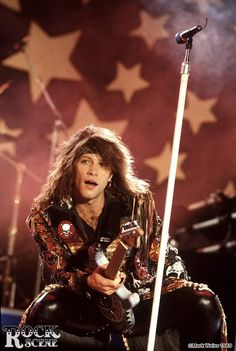 a man with long hair sitting in front of a microphone and holding an electric guitar