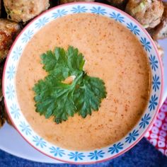 there is a bowl of soup with parsley on the top and meatballs in the background