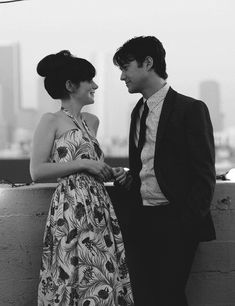 a man and woman standing next to each other on top of a roof looking at each other