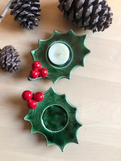 two green dishes with red berries on them next to pine cones and candlesticks