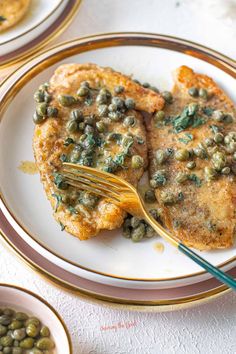 two white plates topped with fish covered in sauce and green beans next to silverware