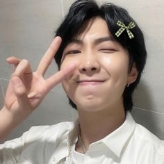 a young man making the peace sign with his hand while wearing a white shirt and green bow tie