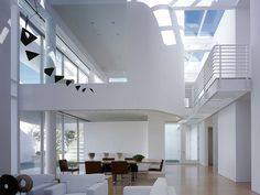 a living room filled with white furniture next to a tall window covered ceiling and wooden flooring