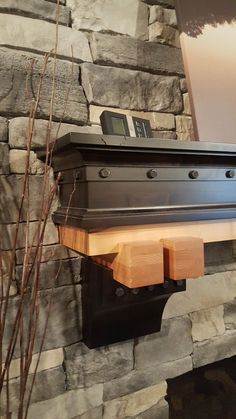 a fireplace with a clock on the mantle and some branches in front of it next to a stone wall