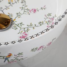 a white sink with flowers and birds painted on the side, next to a gold faucet