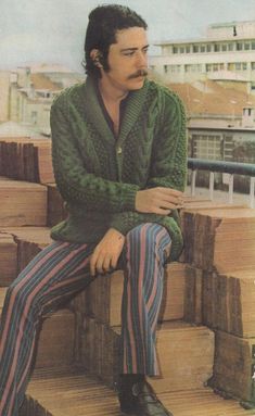 a man sitting on top of wooden steps wearing striped pants and a green cardigan