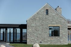 a stone house sitting on top of a lush green field next to a body of water