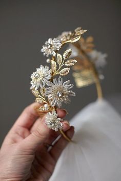 a hand holding a gold and white flower tiara