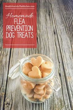 a jar filled with heart shaped dog treats on top of a wooden table next to a red sign that says homemade flea prevention dog treats