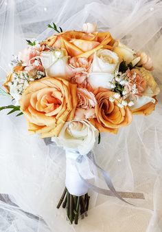 a bridal bouquet with peach and white flowers on a lace tableclothed background