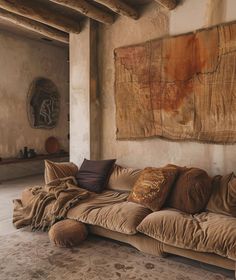 a couch sitting in front of a wall with paintings on it's sides and pillows on the floor