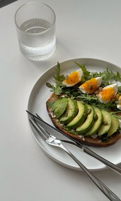 an open face sandwich with avocado, eggs and greens on a white plate