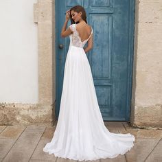 a woman standing in front of a blue door wearing a wedding dress with open back